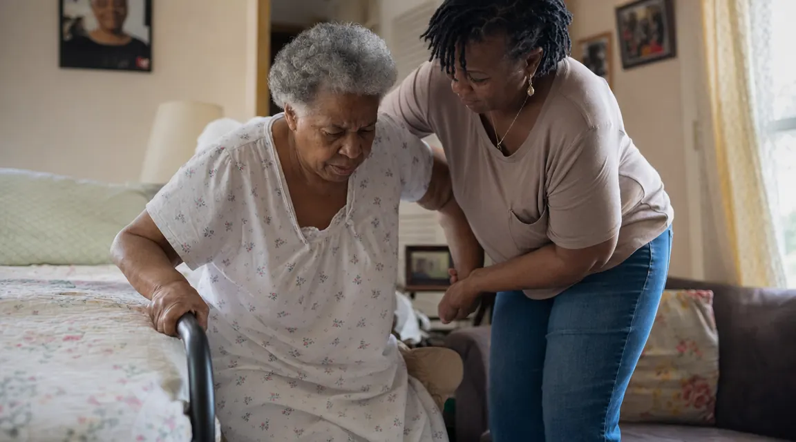Caregiver helping elderly mother stand up from bed using the bed assist bar, both looking relaxed