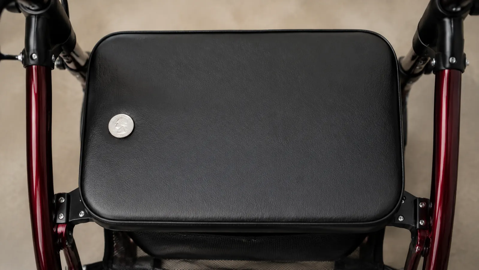 Close-up of a rollator seat showing a thin padded cushion with a quarter coin for scale