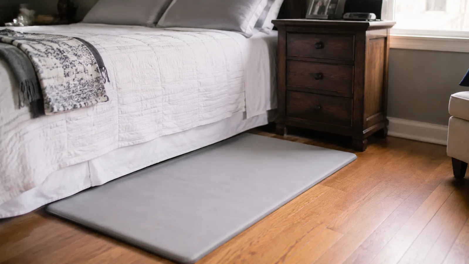 Thin foam fall mat laid flat on hardwood floor beside a bed, showing its low profile against the floor